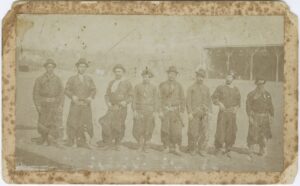 A group of 8 men are standing in a line facing the camera. The photo is black and white and the men are all wearing traditional Argentinian clothing.